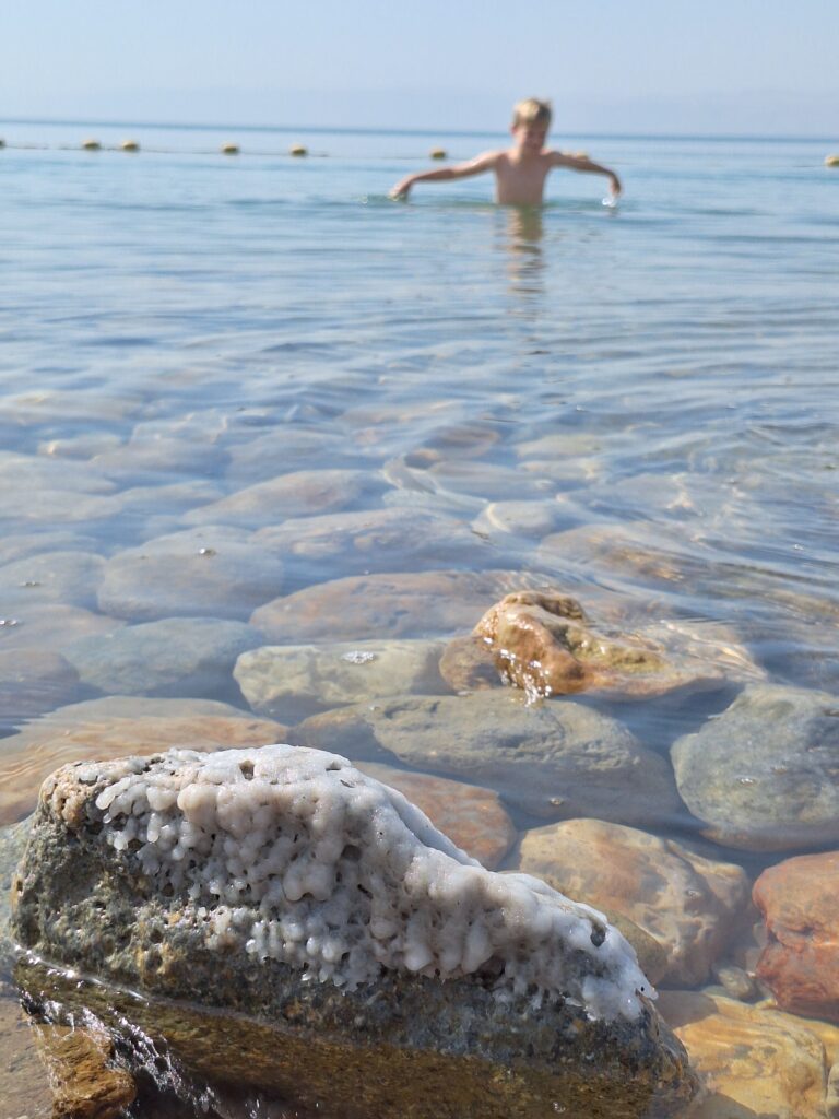 Zoutkristal aan Dode Zee met zwemmende jongen in de achtergrond